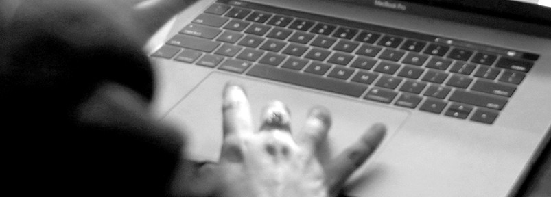 A black and white photo of a person's hand while this person is operating a laptop.